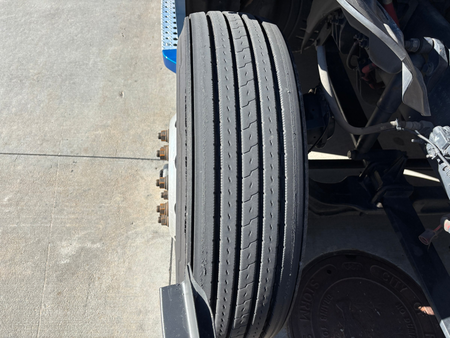 Truck front dual front tire view with wheel studs and suspension components visible; tread marks on tire and surrounding chassis