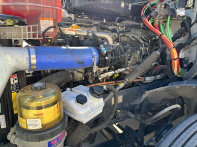 Truck engine bay with blue intake hose, coolant reservoir, oil filter, and wiring harnesses visible.