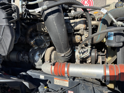 Truck engine bay showing intake hose, belts, and orange coolant hose with warning label.