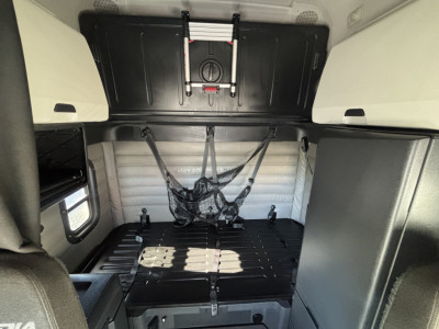 Freightliner PT126064ST sleeper cab interior showing storage area and tie-downs with black panels and light gray upholstery.