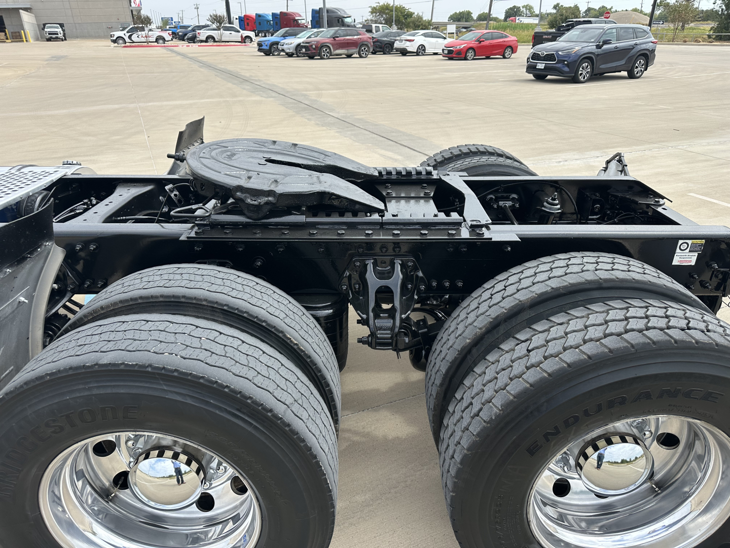 Kenworth truck chassis showing dual rear axles and wheels with chrome hubs and spare components on frame.
