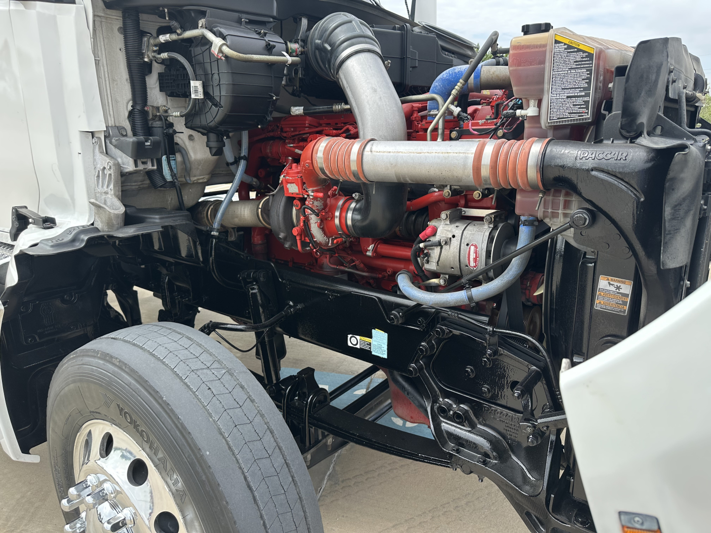 Kenworth T880 engine bay view showing red engine block, intake piping, hoses, and radiator area.