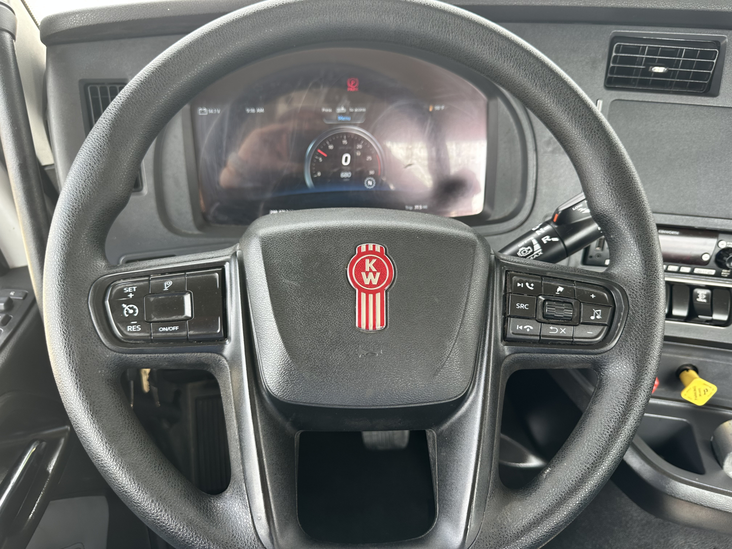 Steering wheel of a 2022 Kenworth T880 cab with KW logo, dashboard display visible behind wheel showing digital gauges and controls.