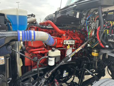 Kenworth T880 engine bay showing Cummins X15 engine with red block and blue intercooler hose, various hoses and wiring present.