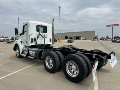 Kenworth T880 sleeper cab tractor rear chassis with dual rear axles and tires, registration tags visible, Kenworth dealership in background.