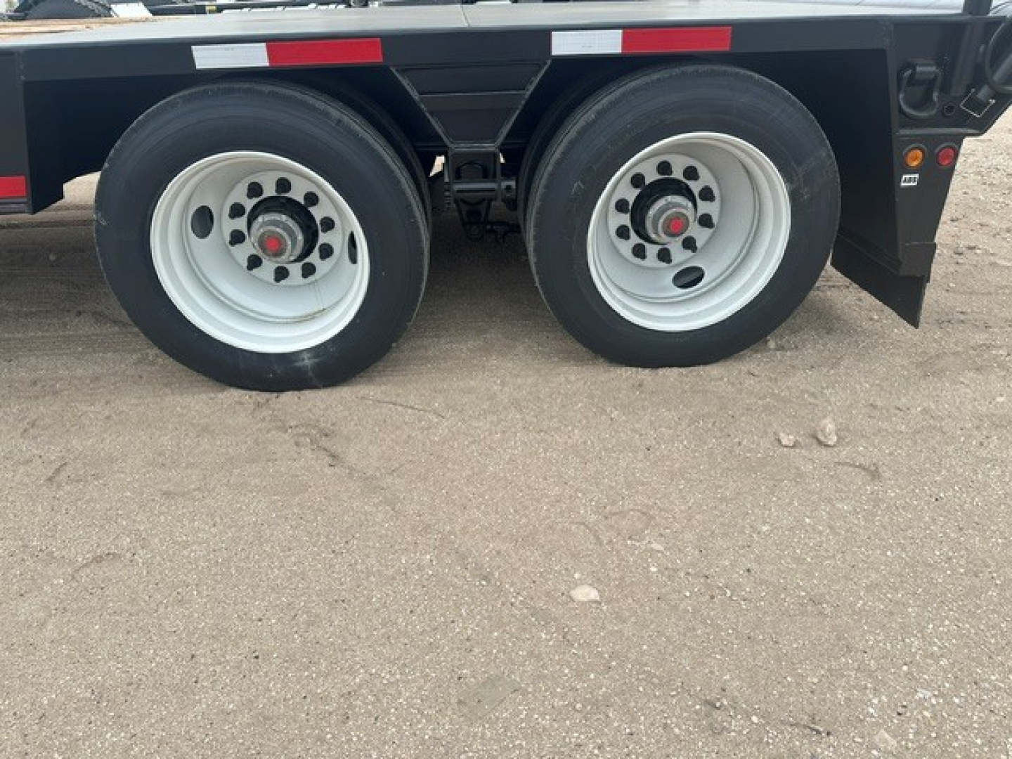 Dual trailer wheels shown on a lowboy trailer with white rims and black fenders.