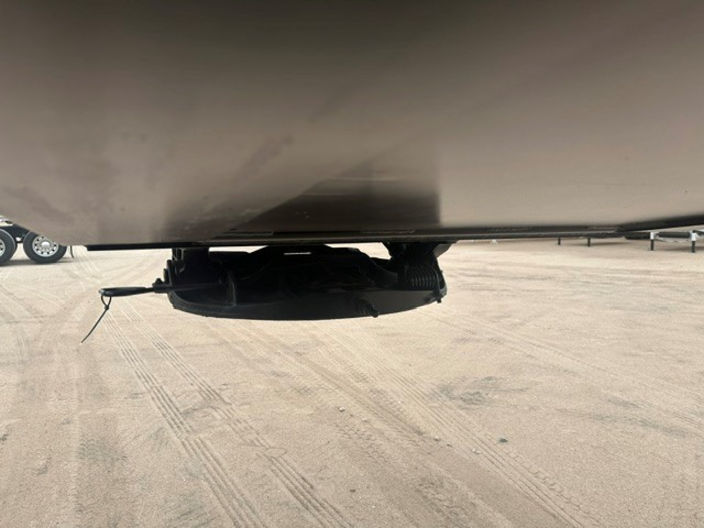 Trailer underside view showing a black hitch component and suspension elements under a lowboy trailer.
