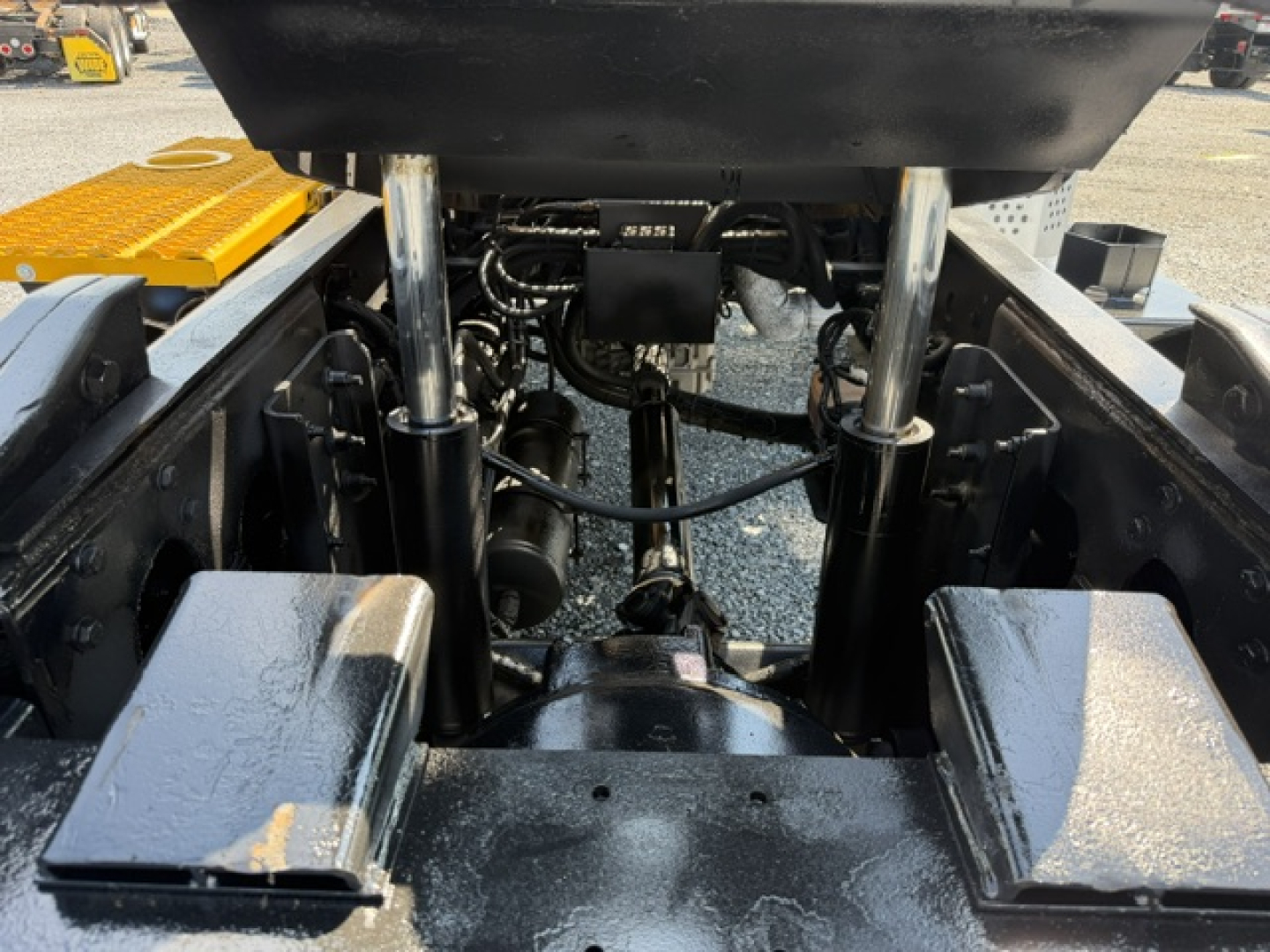 Tractor-trailer truck chassis showing hydraulic cylinders and undercarriage with hoses and components; some labels visible on components.