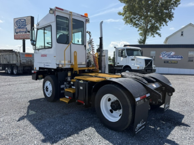 Truck tractor in yard showing cab with yellow steps and white body, rear chassis, and fifth wheel coupling. Visible text includes Sabre on cab and Best Up Trucks sign in background.
