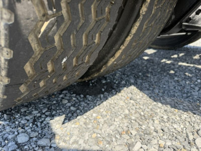 Tire tread close-up on a vehicle wheel showing gravel surface underneath.