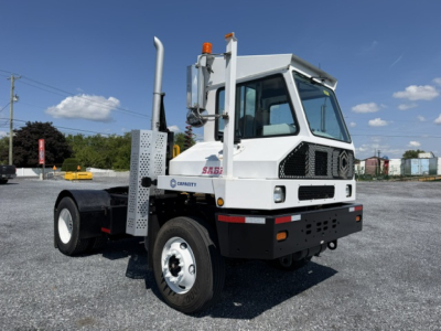 Truck cab side view showing Sabre logo and exhaust stack, front grille, headlights, and off-white body.