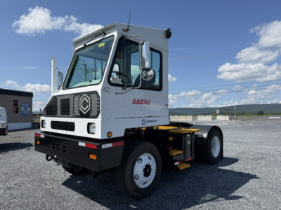 Vehicle cab side showing Sabre yard truck with white cab and black bumper, Sabre logo on door, large front grill, single rear axle configuration.