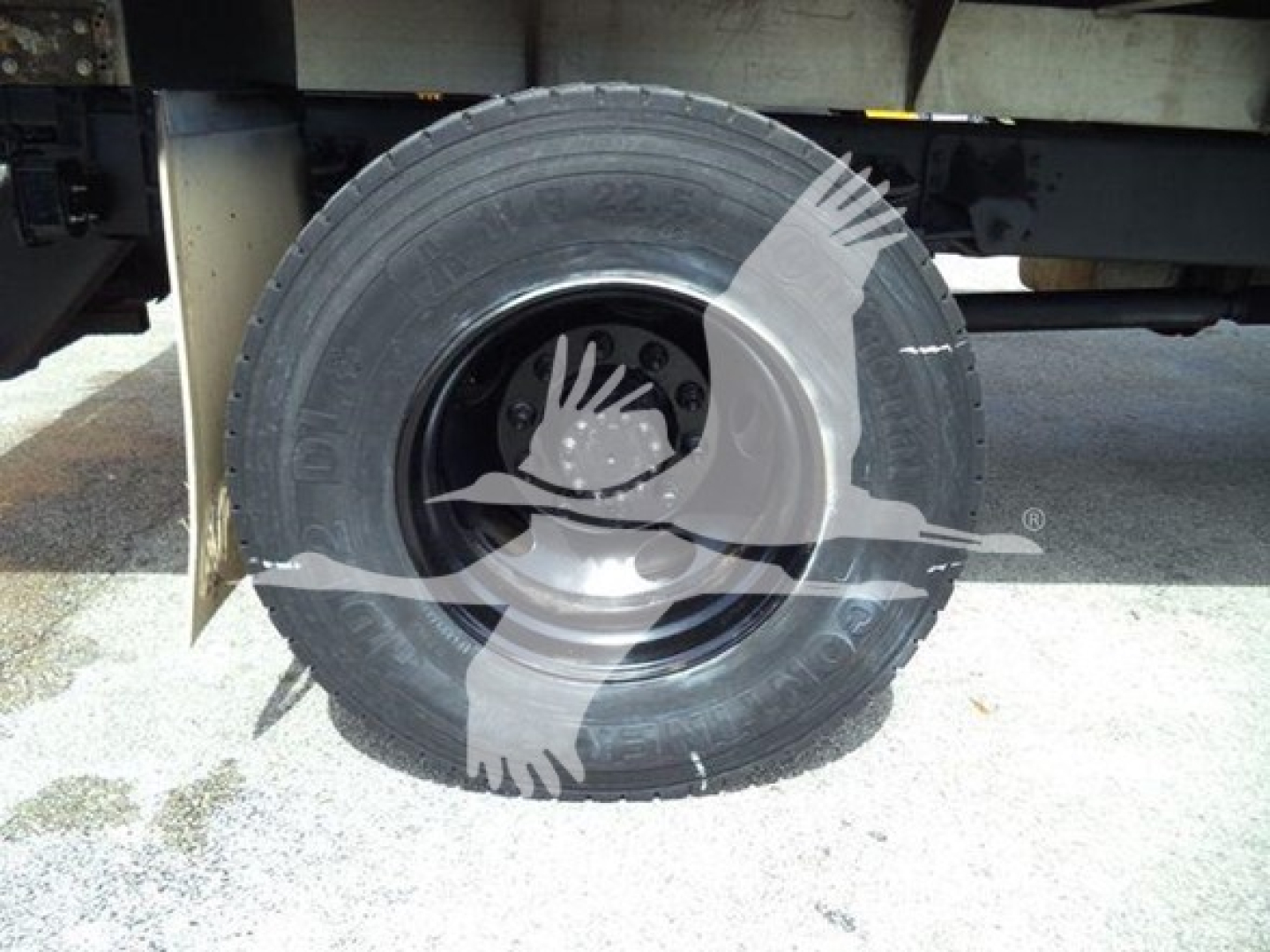Isuzu truck chassis showing a front wheel and tire with spare hub area visible under a chipper truck body.
