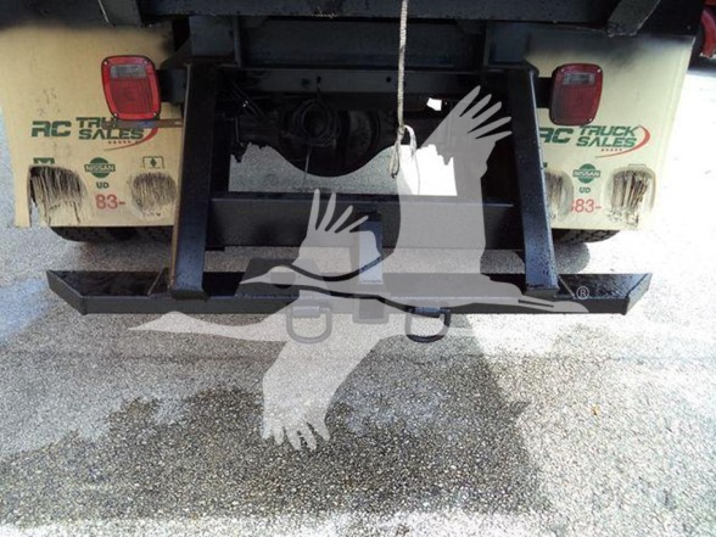 Isuzu truck rear showing hitch and bumper with bumper hitch receiver and taillights; branding on mud flaps reads RC TRUCK SALES; water on ground.