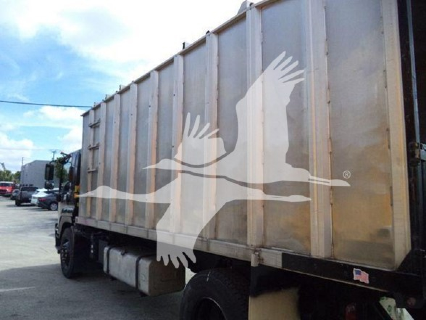 Isuzu truck dump body side view showing large metal cargo hopper with vertical supports and a painted bird silhouette watermark across the image.