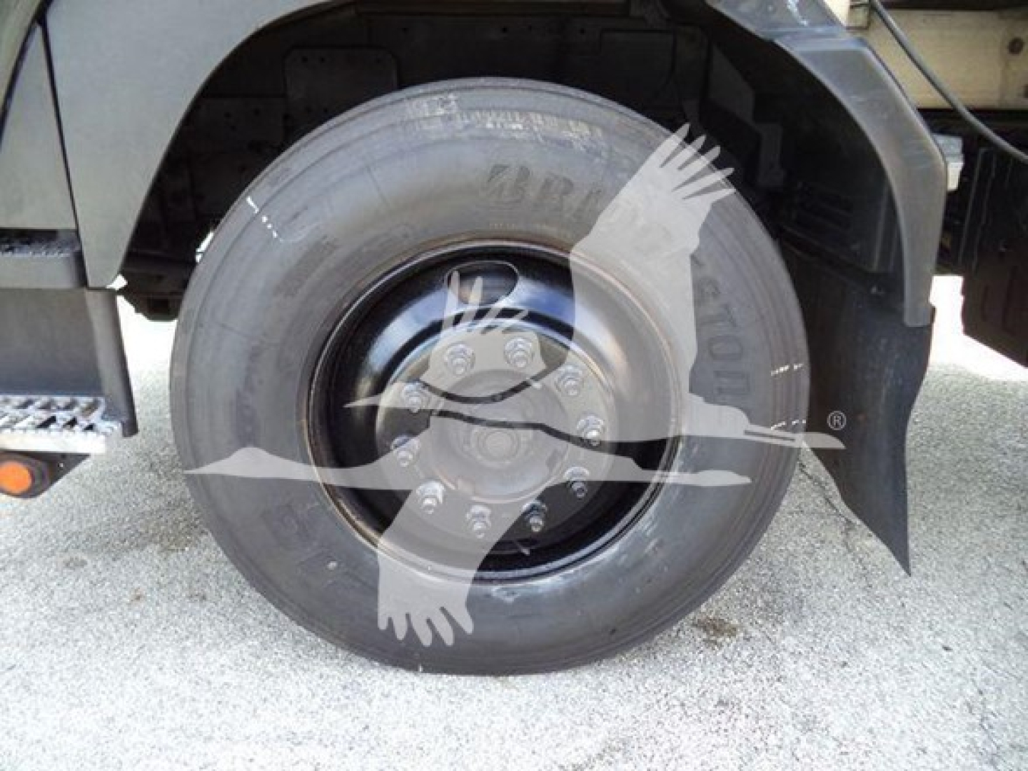 Isuzu truck wheel and front fender view showing single rear tire with solid black rim and fender, part of a chipper truck.