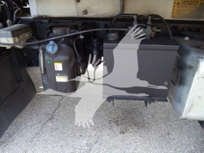 Isuzu truck engine bay area with coolant reservoir and opaque black component; visible labeling on caps and hoses.