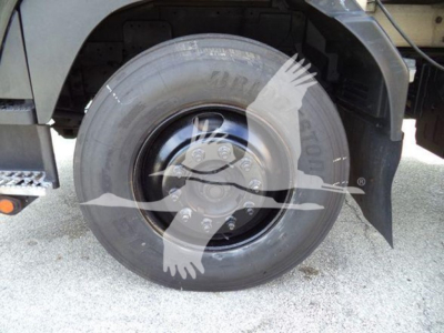 Isuzu truck wheel and front fender view showing single rear tire with solid black rim and fender, part of a chipper truck.