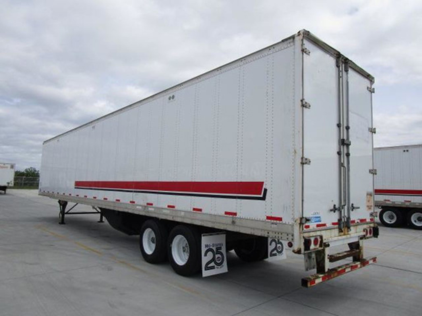 Trailer wagon showing a white Stoughton van trailer with red stripe undercarriage and triple axles in a parking lot.