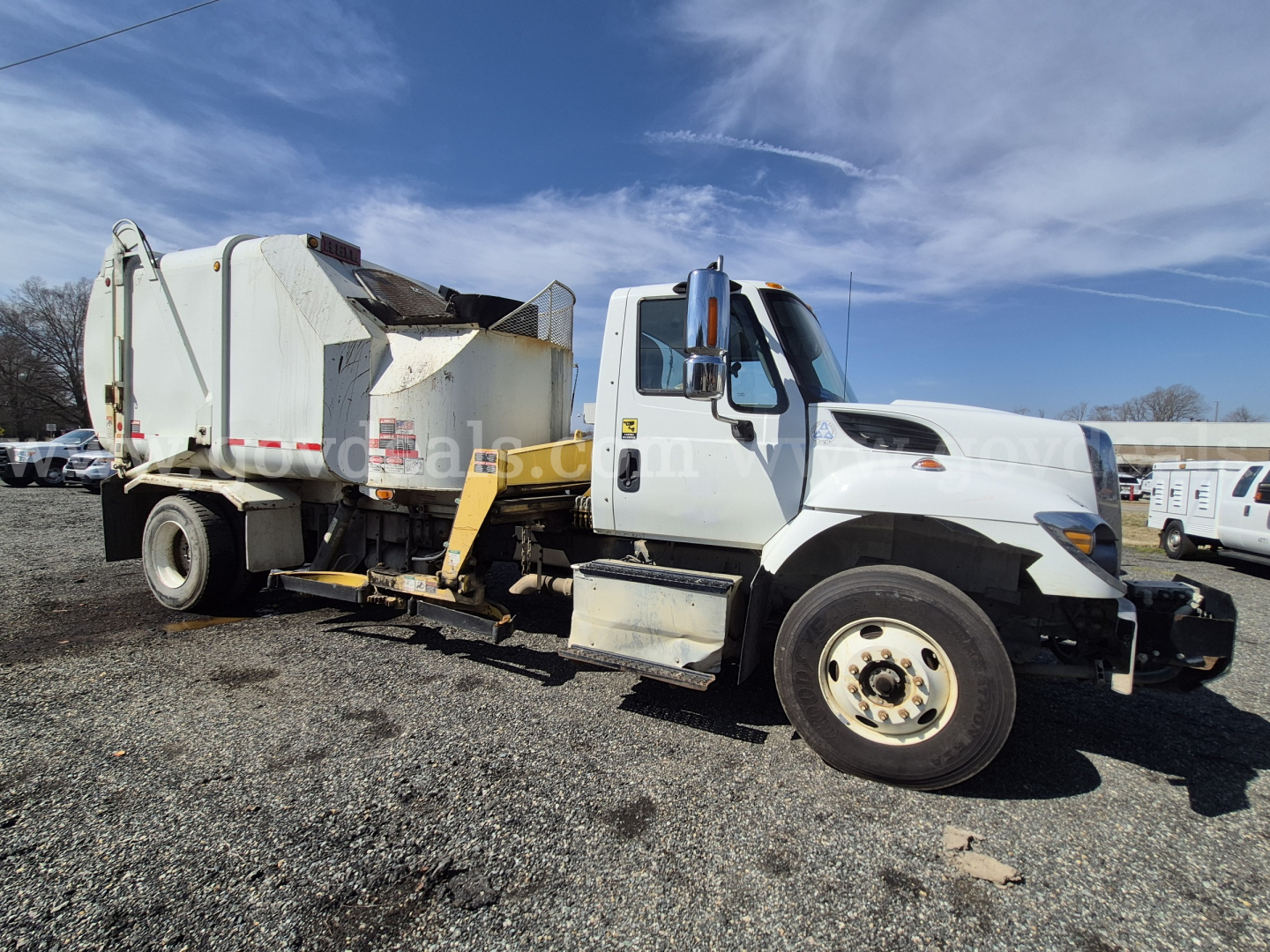 Truck side view of 2017 International 7400 garbage truck showing cab and rear compactor unit with white body and yellow hydraulic arms.