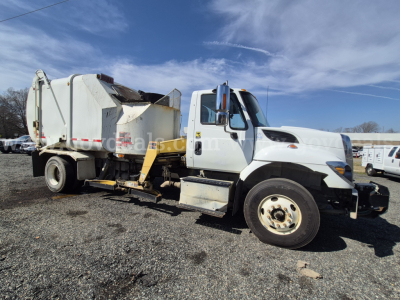 Truck side view of 2017 International 7400 garbage truck showing cab and rear compactor unit with white body and yellow hydraulic arms.