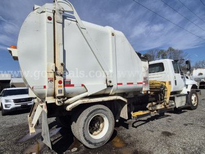 Waste management truck rear and side view showing a large white steel dump body with hinged tailgate, rear bumper steps, and dual rear wheels.