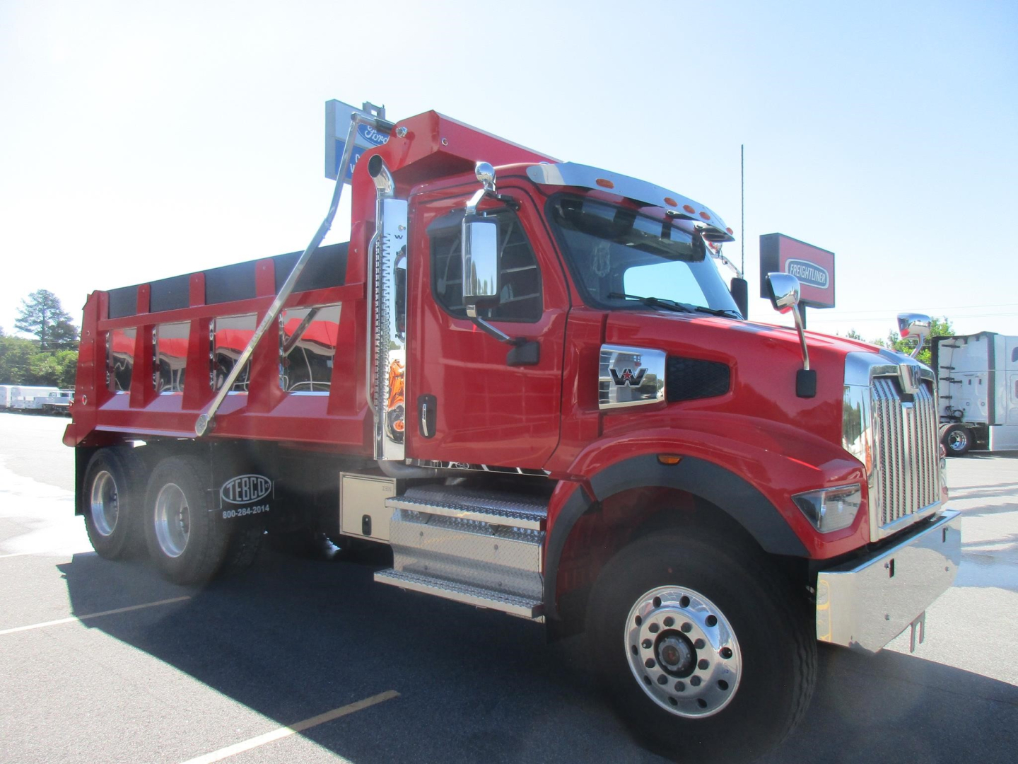 Dump truck in red showing Class 8 Western Star 47X cab with hydraulic dump bed and chrome steps.