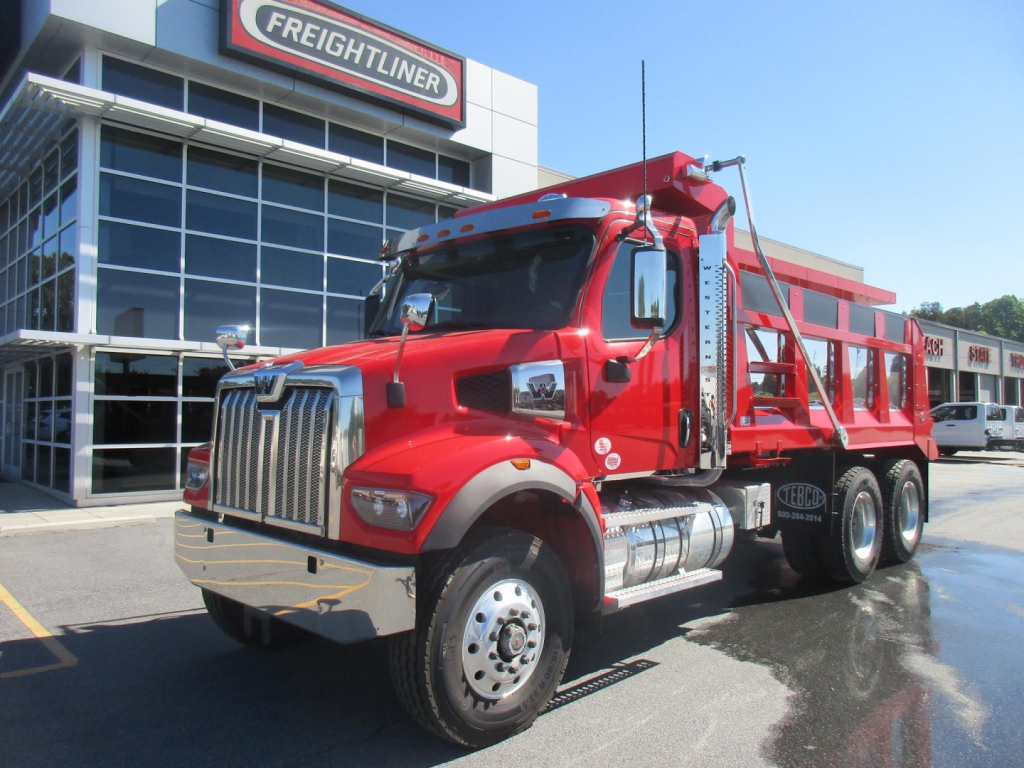 2027 Western Star 47X dump truck in red with chrome grille parked outside dealership; cab and dump body visible.