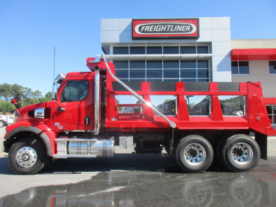 Red Western Star 47X dump truck in profile view parked in lot in front of Freightliner dealership building.