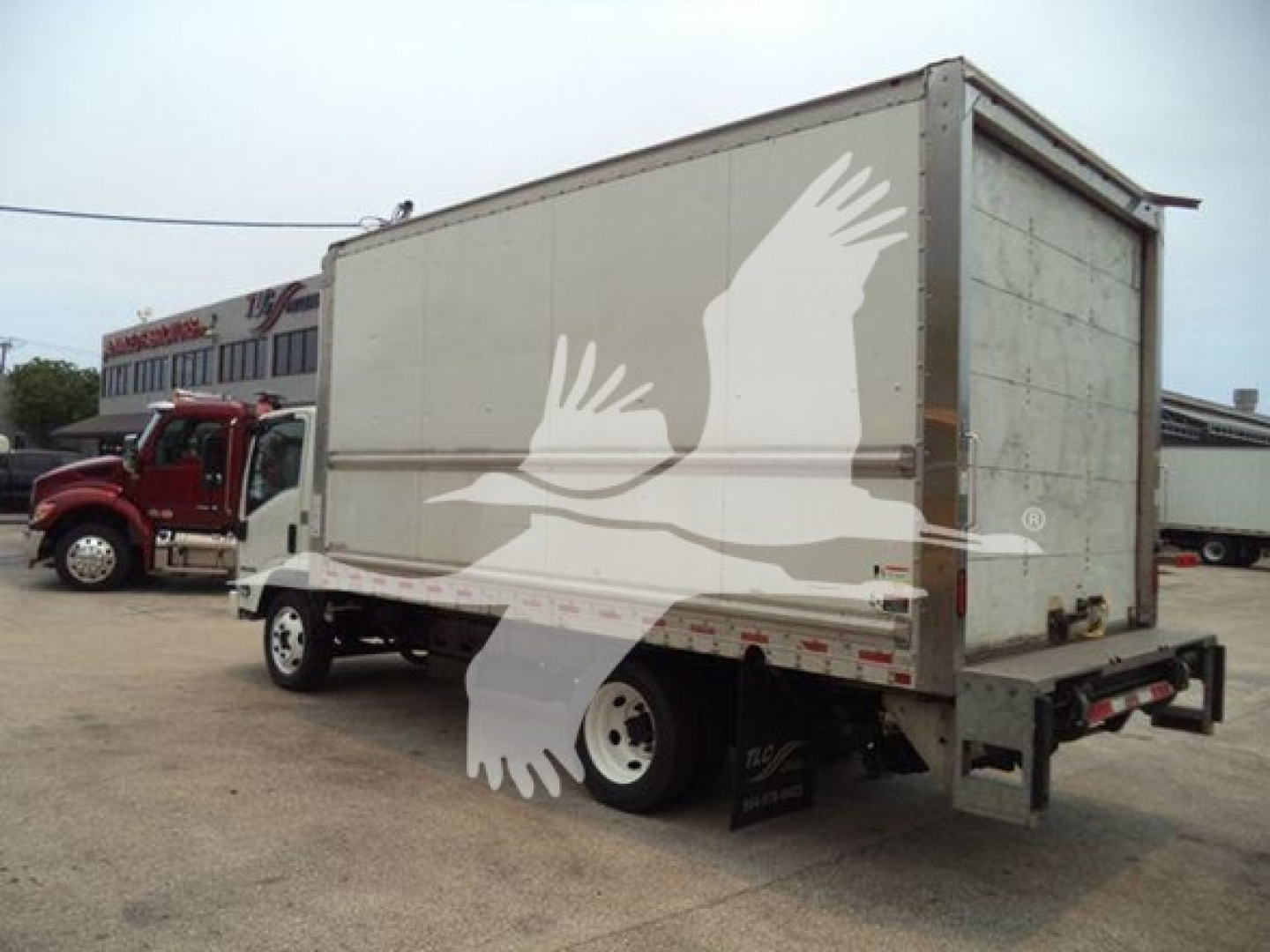 Box truck from rear-left side showing Isuzu NPR-HD cargo box with plain white exterior and metal rear doors.