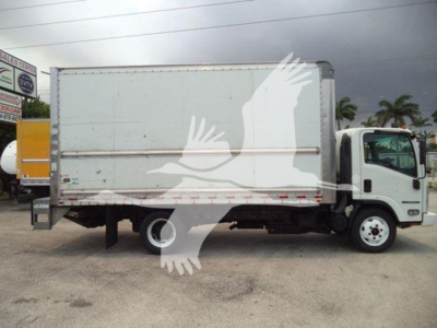 Isuzu NPR HD box truck side view showing cargo box with white exterior and black rear undercarriage, side warning decals, and cab with front wheel visible.