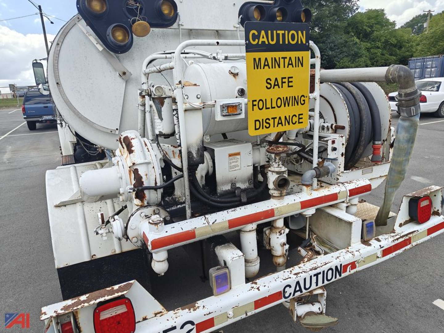 Tanker rear view showing warning sign, piping, and hydraulic components on Freightliner FL70 tank truck rear. Caution labels and reflective edges visible.