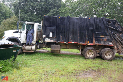 Truck side view showing a white International WorkStar cab with Pak-Mor 30 yard packer body in dark panels parked on grass.