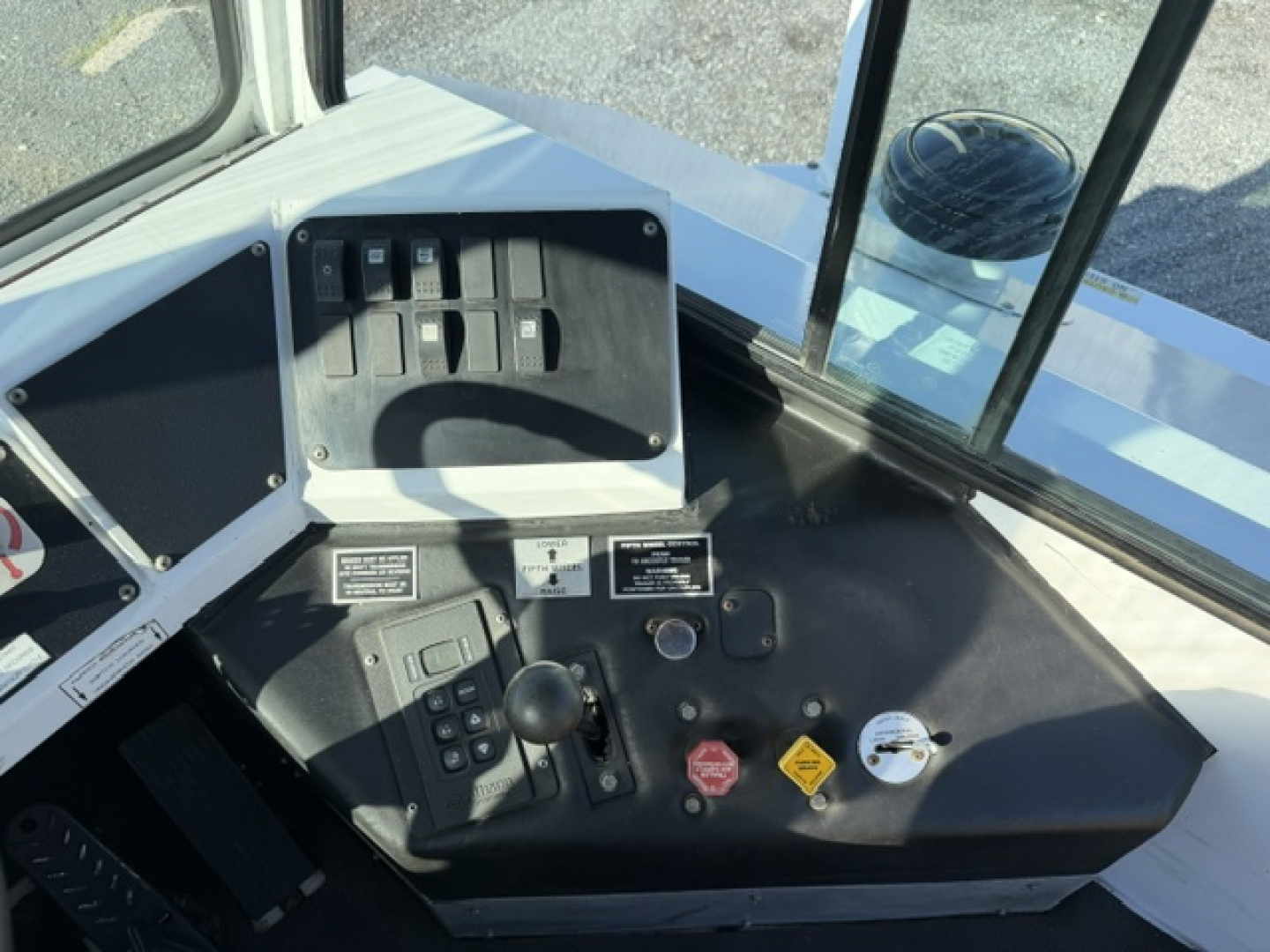 Interior cockpit of a TJ6500 capacity truck showing control panel with switches, gauges, and warning labels. Visible text on panels includes small labels and controls, with a black control console and a red stop button.