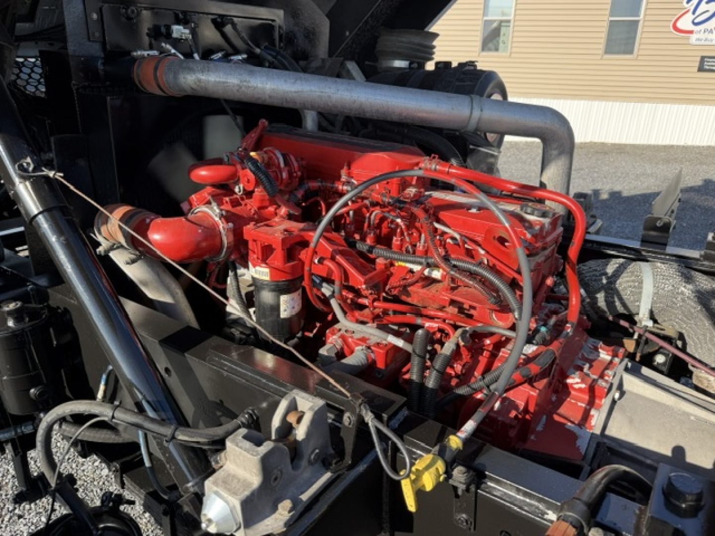 Dual red diesel engine with hoses and metal piping in a truck engine bay. Visible components include red engine block, hoses, and a white label on left side.
