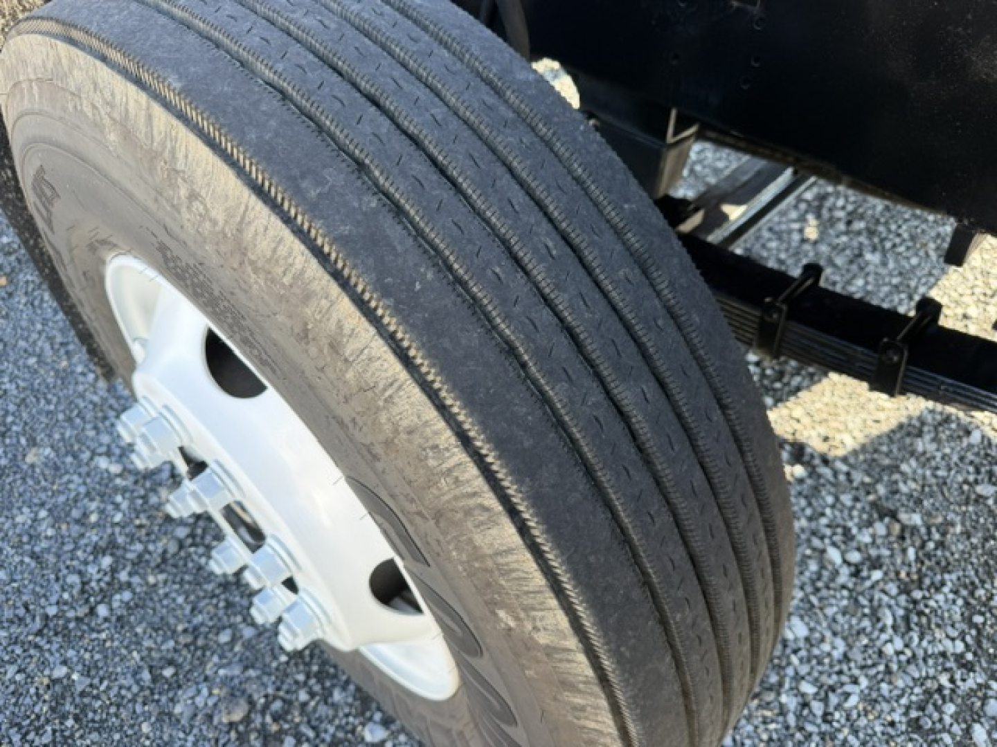 Truck wheel and tire close-up showing single ribbed tread on dual rear axle with white steel wheel and black undercarriage. No visible branding text.
