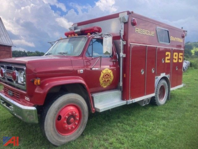 1987 GMC 7000 rescue truck side view showing red fire apparatus with gold rescue emblem and numbers 2 95 on rear quarter, EMS-style door insignia, silver step plates, and emergency lights.