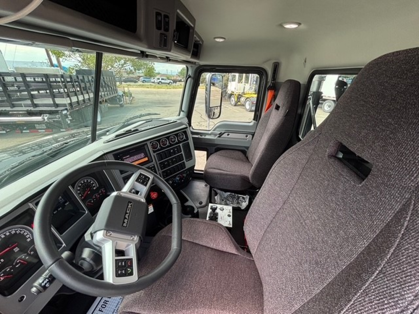 Truck cab interior of a 2026 Mack GR64F showing steering wheel, instrument cluster, center console, and seats.