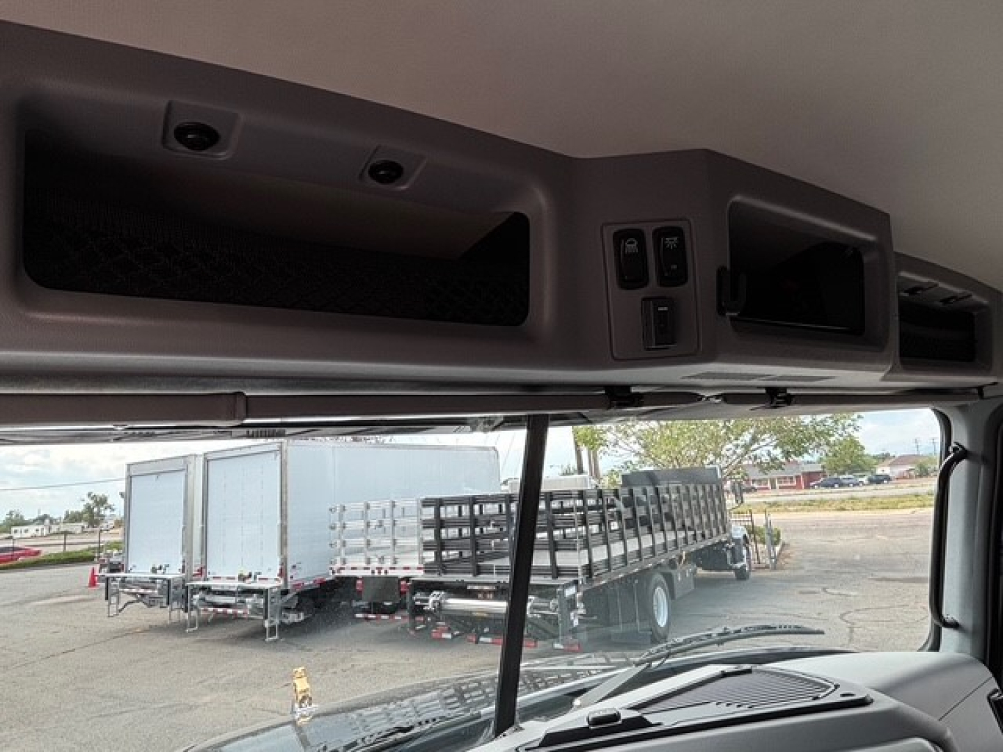 Cab interior overhead controls of a Mack GR64F truck with a view of the dump bed area and the dash; includes window line and exterior lot with trailers.