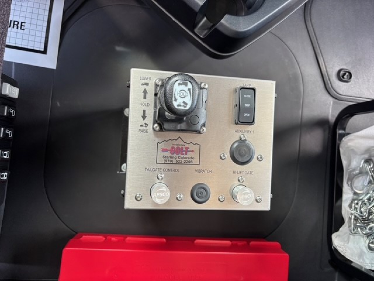 Mack GR64F cab interior showing control panel with toggle, switch, and label; includes lower/raise buttons and DEF-related device; metal square control with circular indicator and small knobs.