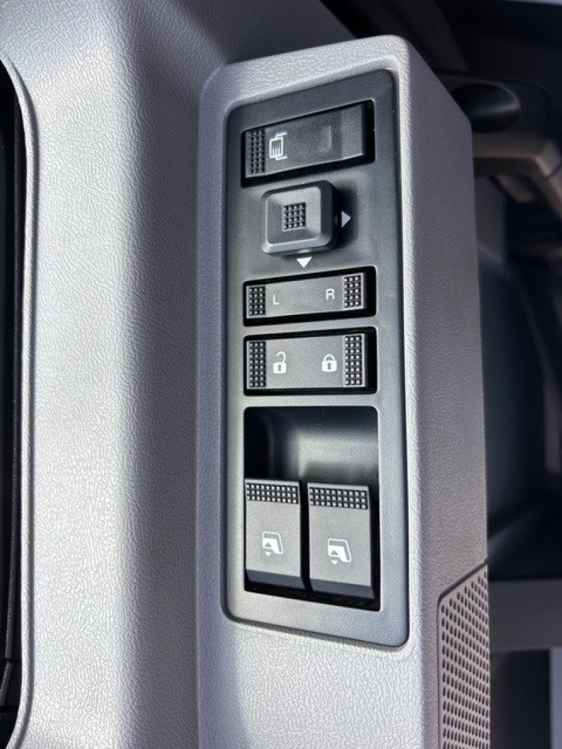Truck interior door panel showing window/lock controls and mirror adjust buttons on a 2026 Mack GR64F cabin. Includes L/R mirror selection, window switches, and lock buttons.
