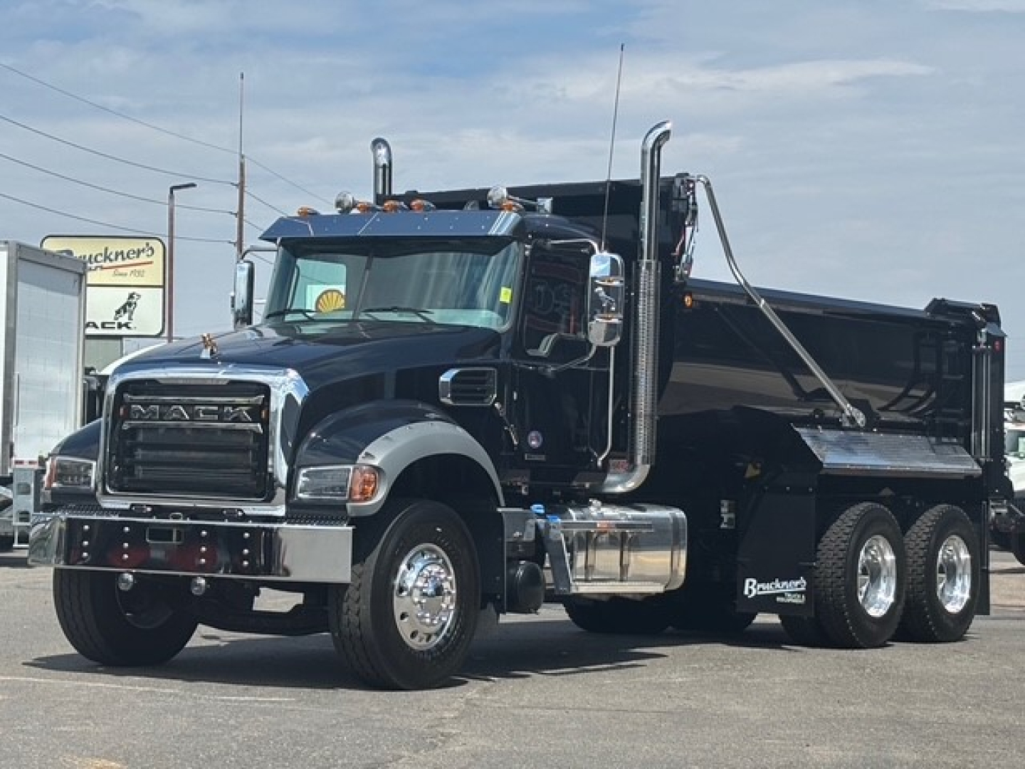 Mack GR64F dump truck in black with chrome grille and dual exhaust stacks, side view showing heavy-duty dump bed and six wheels.