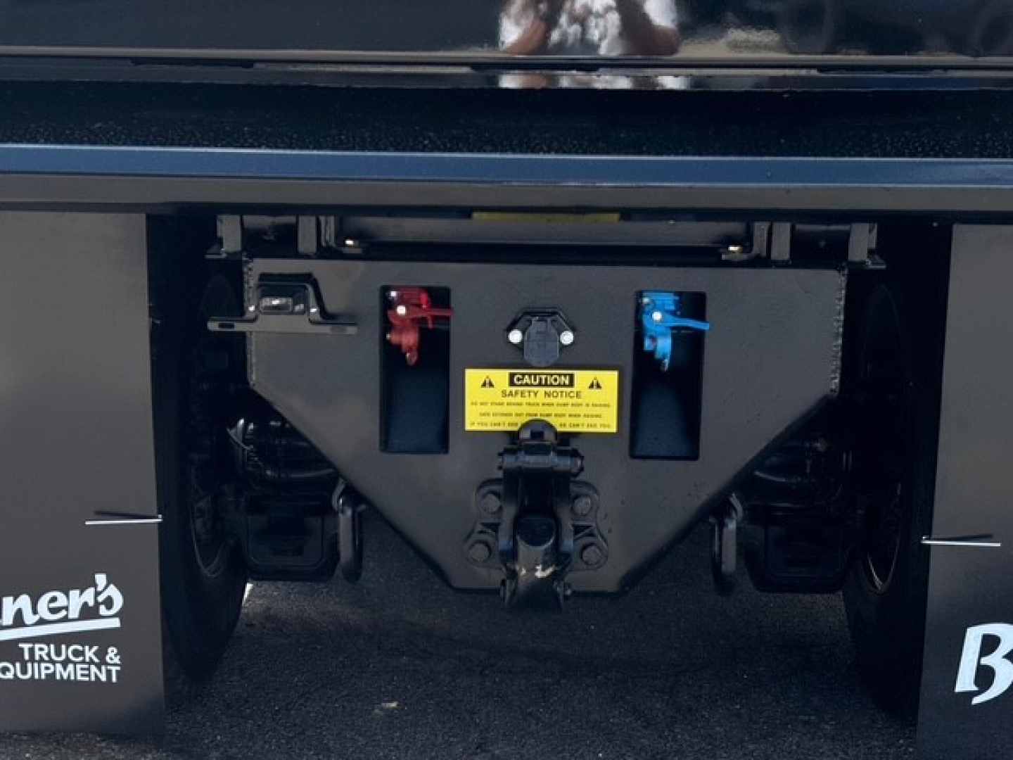 Front rearview of a Mack GR64F dump truck hitch with blue and red battery disconnect levers and a yellow caution label.