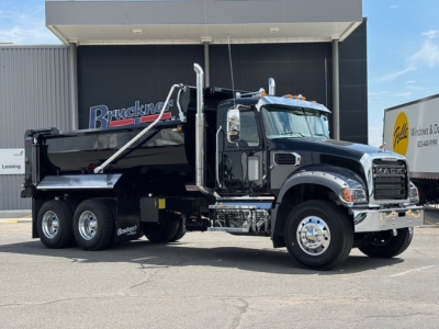 New 2026 Mack GR64F dump truck side view showing black cab with chrome accents and dump bed.