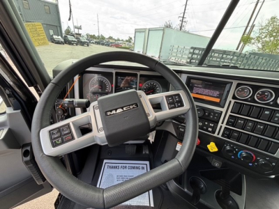 Mack GR64F cab interior with steering wheel and dashboard showing gauges and controls; center console with digital screens and buttons; VIP paper on passenger floor mat.