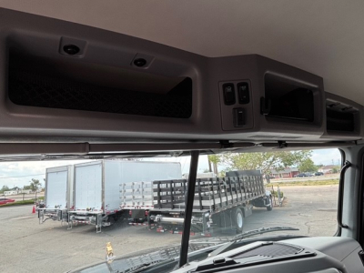 Cab interior overhead controls of a Mack GR64F truck with a view of the dump bed area and the dash; includes window line and exterior lot with trailers.