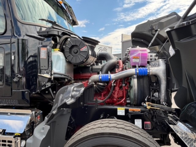 Mack GR64F engine bay showing large turbocharger and coolant reservoirs with hoses and engine components visible.