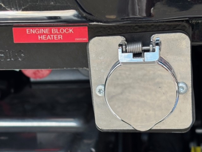 Mack GR64F engine bay rear view showing engine block heater label and circular fuel/connection cap on side.