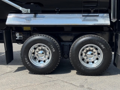 Two rear axles of a Mack GR64F dump truck with dual wheels and chrome hubcaps, diamond plate toolbox above, and heavy-duty tires.