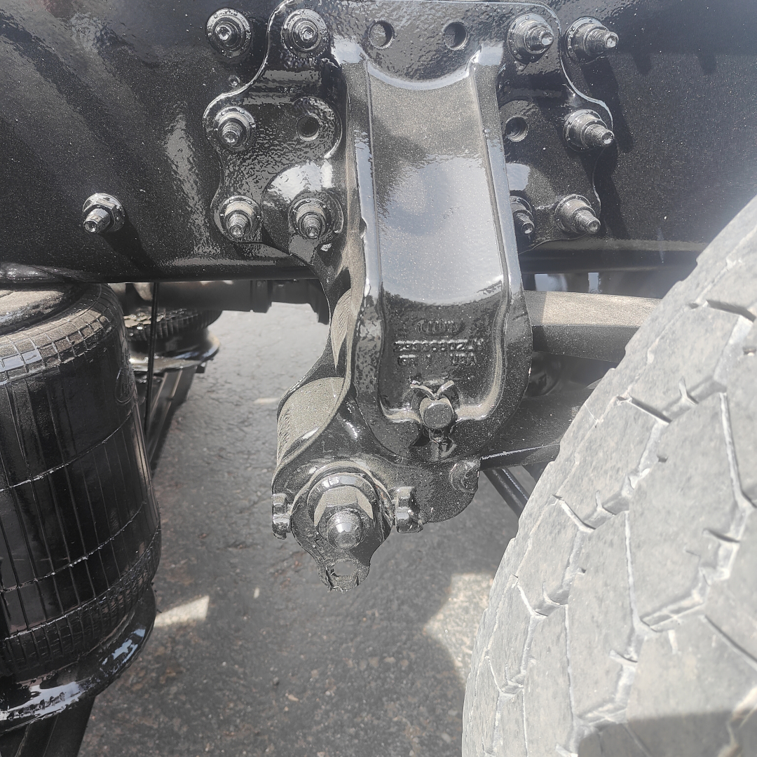 Truck hitch and rear suspension undercarriage with bolts and bracketry, visible air spring canister on left and tire on right.